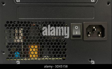 black computer psu back panel with honeycomb mesh vent, power switch and three pin ac socket with internal copper coils and capacitor Stock Photo