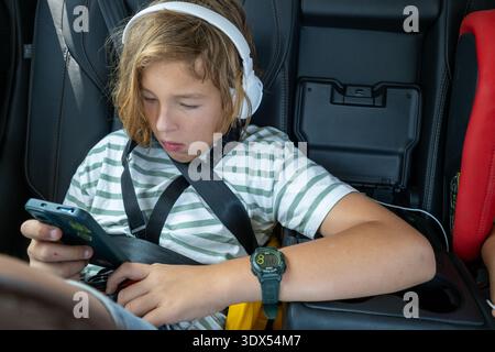 Boy using smartphone in car with headphones Stock Photo