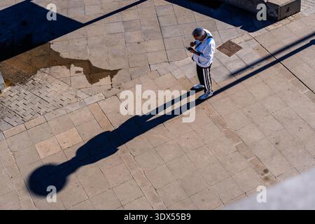 High angle view of a person standing on a concrete plaza with a long morning shadow. Stock Photo