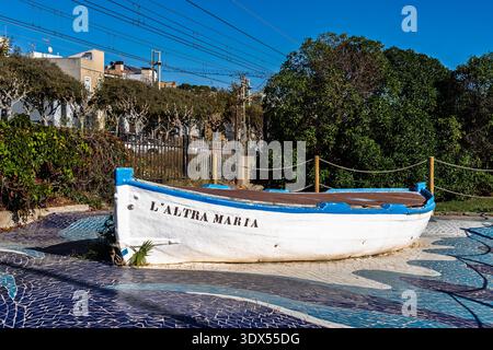 An old traditional wooden fishing boat named L'Altra Maria displayed over a blue wave mosaic in a public park. Badalona, Spain Stock Photo