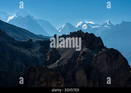 Dhankar Gompa on a ridge with the snow-capped Manirang peak and the Himalayan mountain range in the distance under a clear blue sky. Stock Photo