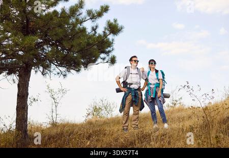Happy hiking couple standing on hill, hikers rest on hillside under pine Stock Photo