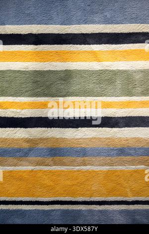 Close-up of textured rug with multicolor horizontal stripes. Detailed fabric fibers and bold bands create vibrant abstract background. Top view. Stock Photo
