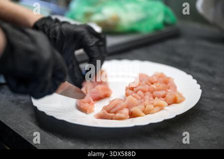 Close view of gloved female hands cutting poultry meat on kitchen surface. Clean food handling concept highlighting preparation, safety, and culinary Stock Photo