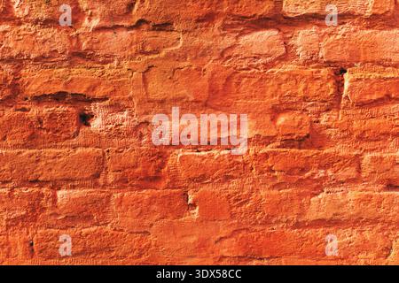 Texture of an aged red brick wall showing uneven mortar lines, deep cracks, chipped edges, subtle black soot marks Stock Photo