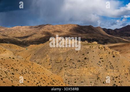 The weathered mud brick ruins of an ancient settlement stand on a ridge above Kaza, set against a dramatic and dark stormy sky in the distance. Stock Photo