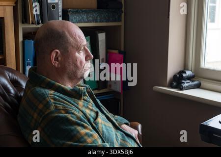 Retired man staring out of a window in contemplation Stock Photo