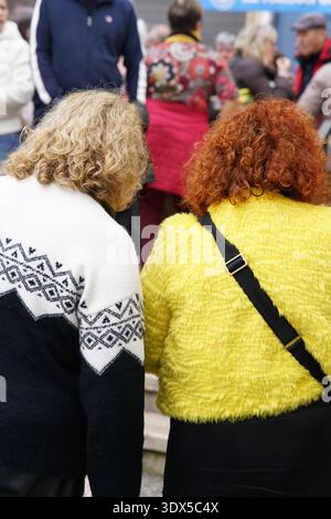 Two women with curly hair in colorful knitwear walk through a lively crowd on a Menton street during market day.Menton,France Stock Photo
