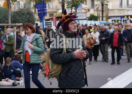 Man in a quirky purple jester hat stands thoughtfully amid the bustling crowd during Menton's festive street event.Menton,France Stock Photo