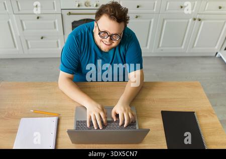 Smiling plus size man with glasses typing on laptop at home kitchen table Stock Photo