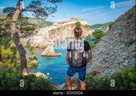 Dubrovnik, Croatia - July 25, 2024: Backpacker Seen from Behind Standing on a Rock at the Viewpoint of Old Fortress in Dubrovnik, Croatia Stock Photo