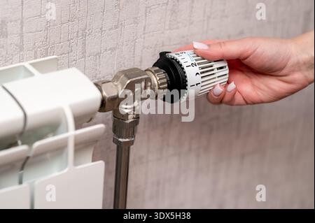A close up shot of a person hand adjusting the thermostatic valve on a home radiator to control the room temperature. Concept of energy efficiency, ho Stock Photo