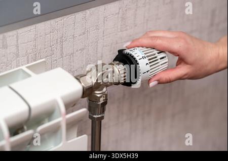 A close up shot of a person hand adjusting the thermostatic valve on a home radiator to control the room temperature. Concept of energy efficiency, ho Stock Photo