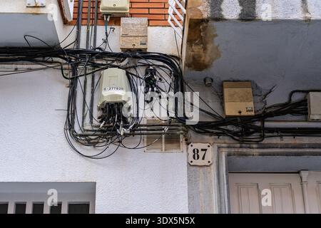 Badalona, Spain - February 3, 2026: Messy bundle of fiber optic and telephone wires connected to junction boxes on an exterior wall next to house numb Stock Photo