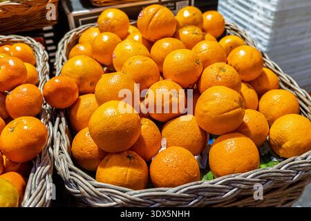 Close-up of ripe oranges piled in woven wicker baskets at a market stall, bright natural light, fresh produce and healthy food concept. Stock Photo