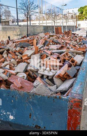 A blue industrial dumpster container filled with construction debris, broken bricks, and concrete from a demolition site. Stock Photo