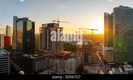 Real estate development in Miami urban area. Tower lifting cranes at high residential apartment building construction site at sunset Stock Photo