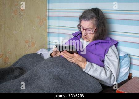 Elderly woman in bed using tablet for communication and comfort at home Stock Photo