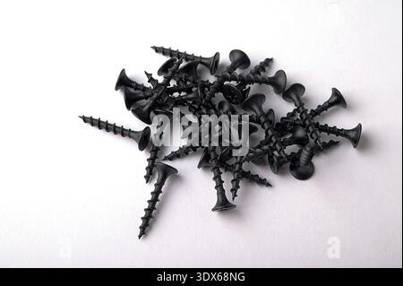 Black self tapping metal, screw white background.Black metal self-tapping screws on wood on a white table. Long black screws on drywall. Stock Photo