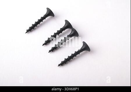 Black self tapping metal, screw white background.Black metal self-tapping screws on wood on a white table. Long black screws on drywall. Stock Photo