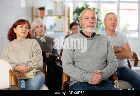 Focused group of students of different ages sitting on chairs and listening lecture in lecture hall Stock Photo