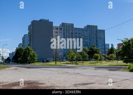 Soviet-era concrete apartment block in Tallinn with beige facade, rows of windows, trees, cars, and a gravel lot under a blue sky Stock Photo