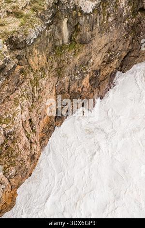 Aerial view of powerful ocean waves crashing against dark coastal rocks ...