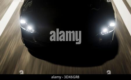 Dark sleek car driving quickly on a road at night, showcasing modern design and advanced lighting technology Stock Photo