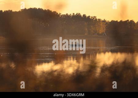 A solitary boat gently floats on Dzirnezers lake under the warm glow of a sunset, capturing the serene beauty of Latvian nature with tranquil waters a Stock Photo
