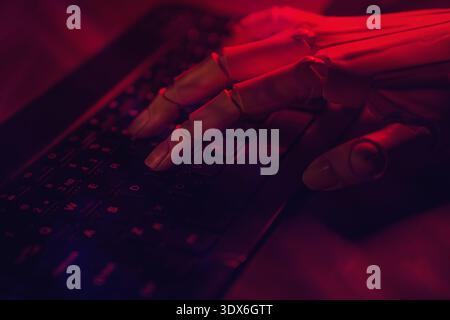 A robotic hand gracefully types on a dimly lit keyboard under a red glow, symbolizing innovation in artificial intelligence and automation technology. Stock Photo