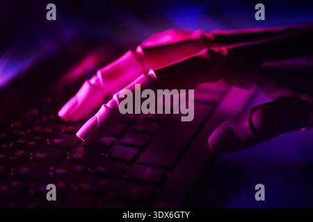 A robotic hand gently rests on a keyboard, illuminated by dim purple light, symbolizing the connection between artificial intelligence and modern tech Stock Photo