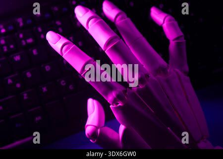 A close-up of a robotic hand with purple lighting rests on a keyboard, symbolizing artificial intelligence and technology. The scene exudes a futurist Stock Photo