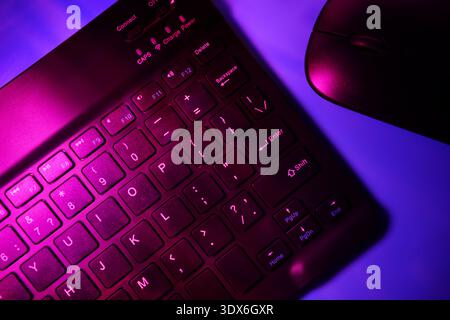 A close-up image of a keyboard and mouse illuminated by vibrant neon lighting, creating a futuristic atmosphere ideal for themes related to technology Stock Photo