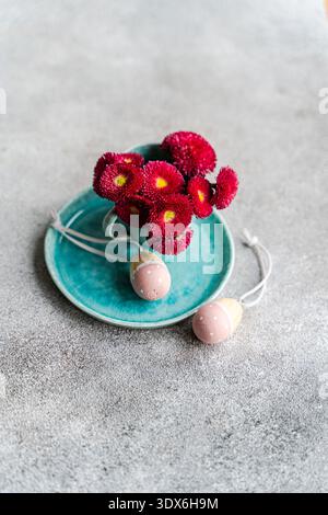 A vibrant spring table setting features a bright blue plate with a decorative flower arrangement. Two pastel Easter eggs add a festive touch, perfect Stock Photo
