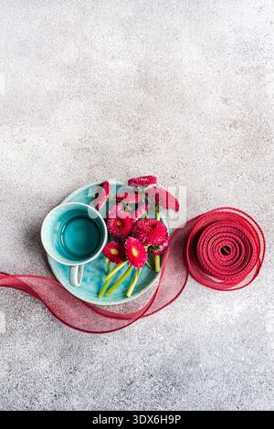 A vibrant spring table setting features a turquoise cup and plate adorned with fresh pink flowers, complemented by a matching decorative ribbon, creat Stock Photo