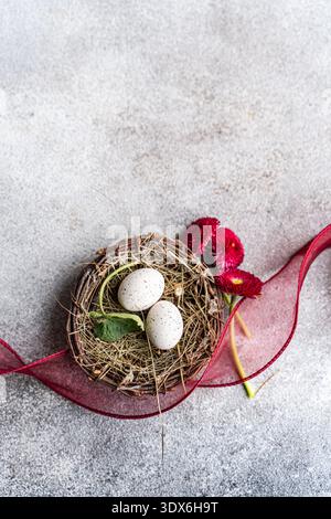 A charming Easter table setting featuring a rustic bird's nest with speckled eggs, surrounded by fresh red flowers and a delicate ribbon, celebrating Stock Photo