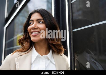 Confident Hispanic businesswoman with Colombian heritage smiling while standing outdoors in a city setting. She exudes professionalism and optimism in Stock Photo