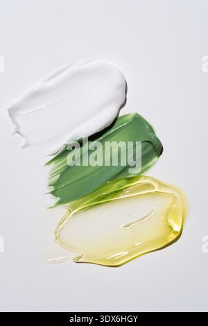 Close-up of three cosmetic product samples with different textures and colors, including white cream, green gel, and yellow serum, displayed on a smoo Stock Photo