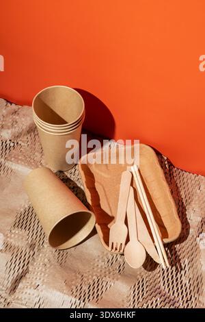 A collection of eco-friendly disposable dishes, tableware, and utensils displayed on a patterned surface. Includes cups, a tray, and wooden cutlery on Stock Photo