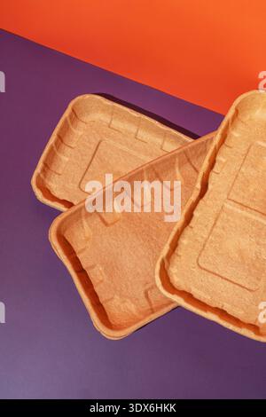 Biodegradable disposable dishes made from eco-friendly materials, set against a vibrant purple and orange backdrop. Perfect for sustainable dining and Stock Photo
