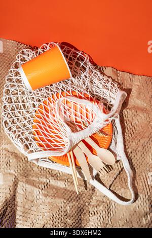Eco-friendly disposable tableware in vibrant orange includes plates, a cup, and wooden utensils. Perfect for casual dining, picnics, and outdoor event Stock Photo
