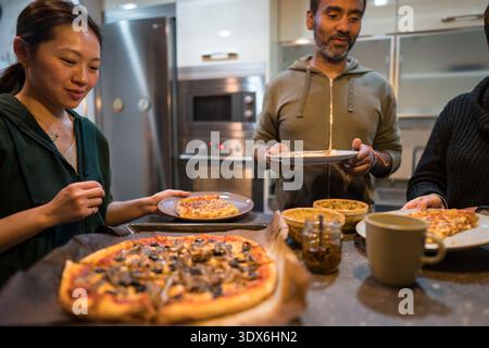 Interracial couple in a cozy kitchen setting, enjoying freshly baked homemade pizza. They share a warm and friendly atmosphere while preparing and ser Stock Photo