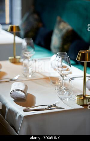 A close-up view of an elegantly set table in a gourmet restaurant, featuring polished cutlery, crystal wine glasses, and cozy ambient lighting, creati Stock Photo
