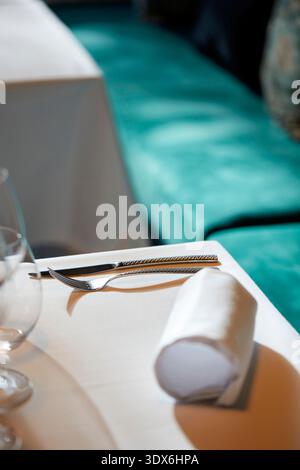A pristine table setting in a gourmet restaurant featuring a neatly arranged fork and knife, a rolled napkin, and a sparkling wine glass, ready for an Stock Photo