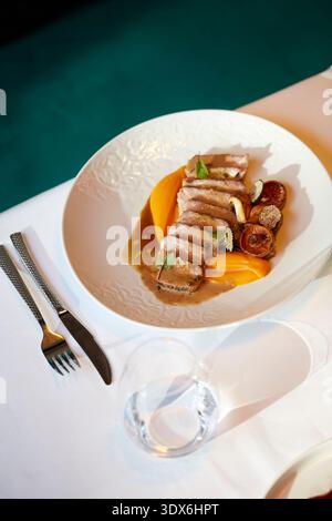 A gourmet dish is elegantly presented on a white plate, set on a crisp white tablecloth. This culinary masterpiece captures the essence of fine dining Stock Photo