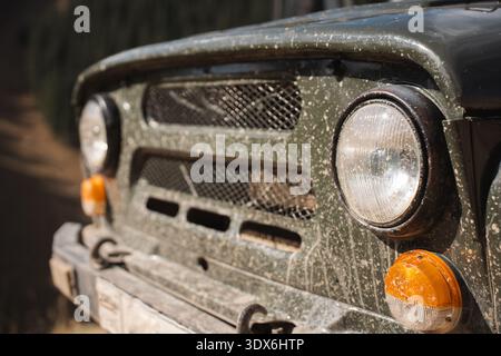 Close up of a vintage off road vehicle covered in mud and dust on a mountain trail in Kyrgyzstan. Headlight and grille detail reflecting rugged outdoo Stock Photo