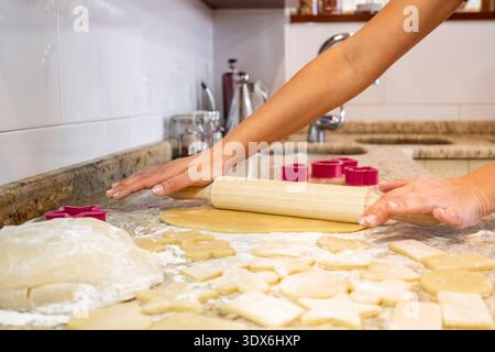 Hands skillfully rolling out dough on a countertop, surrounded by cookie cutters and flour. The scene captures the joy of baking homemade cookies at h Stock Photo