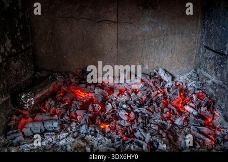 Close-up of glowing red embers and grey ashes in a fireplace, emitting warmth and light. The vibrant coals provide a cozy ambiance, perfect for a warm Stock Photo