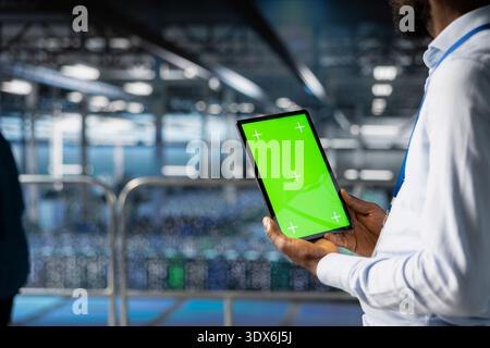 Server room specialist on industrial platform has isolated mockup on tablet, handling optimization tasks in the data center with server racks. Professional visualizing system performance. Stock Photo
