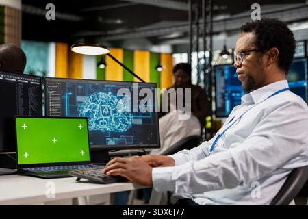 Green screen laptop used by system administrator running AI algorithms in startup workspace. African american man using artificial intelligence deep learning coding platform on mockup notebook Stock Photo